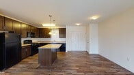 Located at 33 Abbey Lane in Danbury, Connecticut, this single-floor residence offers a thoughtfully designed open-concept layout that seamlessly connects the kitchen, dining, and living areas. The kitchen is a standout feature, showcasing rich dark-espresso cabinetry that extends to the upper walls, light-toned countertops, and a full suite of black appliances including a gas range, built-in microwave, dishwasher, and refrigerator. A central island with pendant lighting overhead provides additional prep space and serves as a natural gathering point. Warm hardwood-style flooring runs throughout the kitchen and main living area, transitioning to plush carpet in the living room and bedrooms.

The living area is generously proportioned and benefits from a sliding glass door that opens to a balcony, allowing natural light to fill the space. The bedrooms are bright and comfortable, each featuring large windows with outdoor views of the surrounding neighborhood and soft carpeted floors. The bathroom is finished with a dark vanity, white countertop, a large mirror, tile flooring, and a full tub-shower combination. The overall aesthetic is clean and contemporary, offering a comfortable and functional living environment.