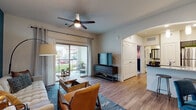 This single-floor residence offers a thoughtfully designed open-concept layout that seamlessly connects the living, dining, and kitchen areas. The living room is anchored by wood-look flooring, a ceiling fan, and a bold teal accent wall, with a sliding glass door that opens to a private patio overlooking a lush green outdoor area, filling the space with natural light. The kitchen is a standout feature, showcasing rich dark cabinetry, granite-style countertops, a subway tile backsplash, stainless steel appliances including a refrigerator, range, microwave, and dishwasher, and elegant pendant lighting above a peninsula with a sink. The dining area provides an intimate setting with its own accent wall detail and decorative touches. The bedroom is a comfortable retreat, highlighted by plush carpet, a patterned feature wall, large windows with blinds, and warm ambient lighting. The bathroom is finished with granite countertops, dark wood-tone cabinetry, a large framed mirror, and a full shower-tub combination. Throughout the residence, consistent wood-look flooring, neutral tones, and modern fixtures create a cohesive and inviting atmosphere suited for contemporary living.