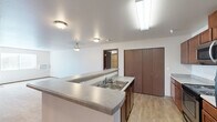 Located in Spokane, WA, this well-appointed two-bedroom, two-bathroom residence offers a comfortable and functional layout across a generously sized single floor. The entrance leads into an open-concept kitchen and living area, where light-toned luxury vinyl plank flooring flows throughout. The kitchen is equipped with stainless steel appliances—including a refrigerator, range, microwave, and dishwasher—complemented by rich dark-wood cabinetry, ample counter space, and a peninsula with a double-basin sink that overlooks the living area, making it ideal for both cooking and entertaining. The living room is carpeted and features a window and direct access to a private balcony. Both bedrooms are carpeted, bright with natural light from large windows, and offer views of the surrounding wooded scenery. The spacious primary bedroom features a dedicated walk-in closet with wire shelving. The primary bathroom includes a dual-sink vanity with warm wood cabinetry and a well-lit mirror. A total of four closets throughout the unit provide exceptional storage. Additional conveniences include a dedicated laundry area and in-unit climate control. The overall ambiance is clean, neutral, and move-in ready.