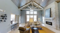 Located at 1431 W Nine Mile Rd in Pensacola, Florida, this single-floor space makes a striking first impression with its dramatic vaulted ceiling adorned with exposed white wood beam trusses and a richly textured wood plank ceiling finish. The open layout is bathed in natural light streaming through a large multi-pane window arrangement, complemented by recessed track lighting that highlights the architectural details above.

The main gathering area is thoughtfully appointed with a sophisticated seating arrangement, anchored by a stone-accented fireplace that serves as a warm focal point along one wall. Soft blue-gray walls create a calm, coastal-inspired ambiance that pairs effortlessly with the light hardwood flooring throughout. A built-in bar or counter area with bar seating is visible to one side, adding a functional and social element to the space.

Large glass doors on either side of the room provide easy access to the exterior, enhancing the flow between indoor and outdoor areas while allowing additional natural light to fill the interior. The overall design blends rustic architectural elements with refined furnishings, resulting in a welcoming and versatile environment well-suited for gathering and community engagement.