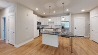 Located at 3925 Senator Royall Dr. in Charlotte, NC, this single-floor residence offers a thoughtfully designed layout with modern finishes and a cohesive neutral color palette throughout. Light wood-tone flooring runs consistently across all rooms, complementing the warm beige and gray tones of the walls and crisp white trim.

The kitchen serves as a central highlight, featuring white shaker-style cabinetry, a classic subway tile backsplash, dark countertops, and a full suite of stainless steel appliances including a refrigerator, range, microwave, and dishwasher. A center island with pendant lighting above provides additional prep space and casual seating, making it ideal for both cooking and entertaining.

The bedrooms are well-proportioned, each equipped with ceiling fans and large windows fitted with blinds that allow generous natural light to fill the rooms. One bedroom includes an attached bath with white cabinetry, dark countertops, and access to a walk-in closet with built-in shelving. An additional bathroom features wood-toned tile accents for a clean, contemporary look.

A spacious open room with double doors and a side-entry door provides flexible use as a living area or additional bedroom. Throughout the space, recessed lighting and abundant natural light enhance the overall bright and welcoming ambiance.