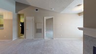 This single-story, one-bedroom, one-bathroom residence offers a thoughtfully designed layout that maximizes functionality and comfort. The living area is a standout space, characterized by vaulted ceilings that lend an open, airy feel. A tiled fireplace with a white mantel serves as a focal point, complemented by a large window fitted with blinds that allows ample natural light to fill the room. Neutral-toned carpet flows throughout the living and bedroom areas, contributing to a warm and cohesive aesthetic.

The kitchen is efficiently arranged with light oak cabinetry providing generous storage, speckled laminate countertops, and black appliances including an electric range and an over-the-range microwave. Adjacent to the kitchen, the layout transitions smoothly toward the bedroom and bathroom.

The bedroom features the same vaulted ceiling design seen in the living area, enhancing the sense of space. It connects directly to the bathroom, which includes a single-sink vanity with a speckled countertop, a large mirror with overhead lighting, and a full tub-shower combination with white tile surround. A closet provides additional storage within the unit.