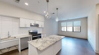 Located at 6300 Clayton Ave in St. Louis, Missouri, this single-floor unit offers a clean, contemporary design throughout. The open-concept kitchen is a standout feature, boasting crisp white shaker cabinetry, a subway tile backsplash, and striking granite countertops on both the perimeter surfaces and a central island. A full suite of stainless steel appliances — including a gas range, dishwasher, and refrigerator — complement the space, while stylish glass pendant lights hang above the island, adding a refined touch. The kitchen flows seamlessly into the living area, which receives natural light through large windows fitted with horizontal blinds. Wide-plank hardwood-style flooring runs consistently throughout the unit, lending a cohesive and modern aesthetic. The bedrooms are bright and well-proportioned, each with windows that bring in natural light and neutral walls that provide a versatile backdrop. Ceiling fans are included in select rooms for added comfort. The bathroom is thoughtfully designed with accessibility in mind, featuring stainless steel grab bars, a wall-mounted vanity with a granite countertop, and a large mirror. The overall ambiance of the unit is fresh, functional, and move-in ready.