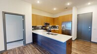 Located at 13325 Station Rail Way in Middletown, KY, this single-floor residence offers a thoughtfully designed layout with modern finishes throughout. The open-concept kitchen serves as the heart of the home, showcasing warm wood cabinetry, a dark subway tile backsplash, stainless steel appliances including a French door refrigerator and microwave, and a striking two-tone island with a white quartz countertop, navy base, and undermount sink with a matte black faucet. Wood-look plank flooring extends through the main living areas, adding warmth and cohesion to the open floor plan. The living area is ceiling fan-equipped and opens directly to a private balcony through sliding glass doors, offering views of the community's expansive courtyard and pool area below. The bedroom features plush carpeting, a ceiling fan, and a large window that frames views of the surrounding modern architecture, filling the room with natural light. The bathroom is finished with white subway tile surrounding the tub-shower combo, matte black fixtures, a granite-topped vanity, and wood-look flooring. Additional highlights include a dedicated in-unit laundry space with a full-size washer and dryer, a walk-in closet with wire shelving, and smart home features such as a digital thermostat and keypad entry.