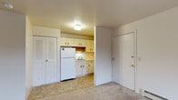 Located at 1057 Mount Royal Dr in Kalamazoo, MI, this single-floor unit offers a straightforward, open layout designed for practical everyday living. The main living area is carpeted and generously sized, featuring a wall-mounted air conditioning unit, baseboard heating, and a large sliding window that fills the space with natural light while providing views of the surrounding landscape. The open layout connects the living area directly to the kitchen, which is efficiently arranged with cream-colored cabinetry featuring wood-tone hardware, a white refrigerator, a gas range, a single-basin stainless steel sink, and ample upper and lower cabinet storage. Under-cabinet lighting above the sink adds functionality to the workspace. A louvered bifold closet door near the entryway provides convenient storage directly off the main living space. The bathroom features tile flooring, a built-in vanity counter with cabinet storage, a towel bar, and clean, neutral-toned walls. The unit's overall palette of cream and white tones throughout creates a cohesive, understated aesthetic that is easy to personalize.