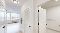 Located at 300 E Main St in Bound Brook, NJ, this studio unit offers a thoughtfully designed, single-floor layout that maximizes every square foot of its compact footprint. The open-plan living and kitchen area is anchored by large windows that flood the space with natural light and offer views of the surrounding neighborhood and landscape beyond.

The kitchen is a standout feature, outfitted with sleek blue-gray cabinetry, a full suite of stainless steel appliances including a range, built-in microwave, dishwasher, and refrigerator, and a clean white countertop with an undermount sink. Track lighting overhead and warm hardwood-style flooring complete the contemporary aesthetic.

The living area is bright and open, with the same hardwood-style flooring continuing throughout, crisp white walls, and a wall-mounted HVAC unit beneath the oversized windows. The entry hallway is well-organized, featuring a louvered closet door and clean panel doors with matte black hardware adding a modern accent.

The bathroom is finished in a crisp, all-white palette with large-format tile flooring, a gray vanity with a white countertop, a wall mirror, and a glass-enclosed shower. Grab bars are thoughtfully incorporated for added accessibility. A dedicated closet with built-in shelving and hanging rod provides practical storage within the living area.
