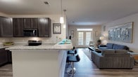 This single-floor residence offers a thoughtfully designed open-concept layout that seamlessly connects the kitchen, dining, and living areas. The kitchen is equipped with dark espresso cabinetry, granite countertops, stainless steel appliances including a refrigerator, range, and microwave, and a breakfast bar with pendant lighting — ideal for casual dining or entertaining. Adjacent to the kitchen, the dedicated dining area accommodates a full-sized table and is accented by a large wall mirror that enhances the sense of space. The living room is bright and inviting, featuring wood-look plank flooring, neutral-toned walls, and French doors that invite natural light and provide access to an outdoor area. Two well-sized bedrooms are finished with plush carpeting and ceiling fans, each offering ample closet space with built-in wire shelving. The two bathrooms mirror the home's design aesthetic, featuring dark vanity cabinetry, light countertops, and wood-look flooring. One bathroom includes a full shower-tub combination. Additional storage is provided throughout, and a laundry area is conveniently accessible. The overall ambiance is clean, modern, and functional, with a cohesive neutral palette accented by warm wood tones throughout.