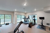 Located at 1550 Perimeter Pkwy NW in Huntsville, Alabama, this well-appointed fitness center offers a comprehensive exercise environment within a thoughtfully designed single-room layout. The space is flooded with natural light through a series of large, floor-to-ceiling windows along multiple walls, providing open views of the surrounding greenery and creating a bright, energizing atmosphere.

The exercise room is equipped with a full suite of cardio machines, including multiple treadmills, an elliptical trainer, a rowing machine, and stationary cycling bikes — one of which features an interactive digital display screen. Strength training needs are well-addressed with a multi-function cable/functional trainer machine, an adjustable weight bench, dual dumbbell rack towers, and an assortment of medicine balls and accessories.

A wall-mounted flat-screen television is positioned for easy viewing during workouts, while a decorative piece of artwork adds a touch of warmth to the otherwise modern aesthetic. Recessed ceiling lighting complements the natural light, ensuring the space remains well-illuminated at all times. The neutral-toned carpet flooring and clean white walls contribute to an uncluttered, professional gym atmosphere. The space also includes a sanitizing station and posted fitness guidelines, reflecting a commitment to cleanliness and user safety.