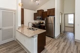 Located in Farragut, Tennessee, this single-floor residence offers a well-designed layout with a clean, contemporary aesthetic throughout. The heart of the home is a striking kitchen with soaring vaulted ceilings, rich dark-wood cabinetry, and light granite countertops extending across both the perimeter counters and a central island with a double stainless steel sink. A full suite of stainless steel appliances — including a refrigerator, range, microwave, and dishwasher — completes the space, while elegant pendant lighting adds a refined touch overhead. Track lighting further illuminates the area, and light wood-style flooring runs seamlessly through the kitchen and living areas, creating a cohesive, open feel. The living area benefits from generous ceiling height and natural light from a large window, with a ceiling fan providing additional comfort. Bedrooms are carpeted and feature tray ceilings with ceiling fans, offering a cozy, well-proportioned retreat. One bedroom includes a walk-in closet. The bathrooms are finished with granite-topped dark wood vanities and wood-style flooring; one includes a tub/shower combination, while another offers a lighted vanity mirror, lending a modern, polished look throughout.