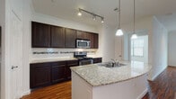 This single-floor residence offers a thoughtfully designed layout that seamlessly blends style and functionality. The kitchen is a standout feature, showcasing rich dark wood cabinetry extending to the ceiling, granite countertops, a decorative tile backsplash, and a full suite of stainless steel appliances including a refrigerator, electric range, and built-in microwave. A peninsula with an integrated double sink and pendant lighting above creates an ideal space for meal prep or casual dining, while track lighting overhead ensures excellent illumination throughout.

The open-concept living area flows naturally from the kitchen, featuring warm hardwood-style flooring, crown molding, and a ceiling fan that adds both comfort and character. Natural light filters in through multiple windows fitted with blinds. The bedrooms are carpeted for comfort, each equipped with ceiling fans and generous natural light from dual windows. A spacious walk-in closet with built-in shelving and hanging rods provides ample storage.

Both bathrooms are finished with granite vanity tops, dark cabinetry, large mirrors, tile flooring, and tub-shower combinations with full tile surrounds, delivering a clean and cohesive aesthetic throughout the home.