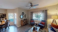 This single-story residence offers a thoughtfully designed layout with distinct living, sleeping, and utility spaces connected by consistent, contemporary finishes throughout. The living room serves as the heart of the home, featuring wood-style plank flooring, a ceiling fan, and a large window dressed with patterned curtains that frame views of outdoor greenery, filling the space with natural light. Decorative mirrors and a rustic multi-drawer console add character to the room.

The kitchen is outfitted with dark wood cabinetry, granite-style countertops, a full suite of white appliances including a range, microwave, and dishwasher, plus a stainless steel sink — offering both functionality and style.

The bedrooms are carpeted for comfort, each featuring ceiling fans and ample closet space. One bedroom includes a walk-in closet, providing generous storage. The bathrooms echo the kitchen's aesthetic with granite countertops, dark cabinetry, framed mirrors, and tub-shower combinations with stylish curtains.

A dedicated laundry area with a full-size washer and dryer adds everyday convenience. The overall ambiance is modern and cohesive, with neutral tones and warm accents creating an inviting atmosphere throughout.