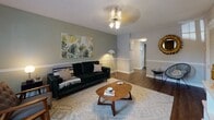 Located at 5039 Chalet Ct in Tampa, Florida, this single-floor residence offers a well-organized layout designed for comfortable everyday living. The living room serves as the heart of the home, featuring warm hardwood-style flooring, a textured ceiling, and a ceiling light fixture. Sage-green walls and tropical botanical wall art lend the space a relaxed, nature-inspired atmosphere, complemented by a mix of seating and a mid-century modern coffee table. An adjacent sitting area provides additional lounging space, complete with hardwood floors, neutral tones, and a large wall-mounted television. The dining area features hardwood-style flooring, chair rail molding, and a sliding door that introduces natural light, creating a bright and welcoming space for meals. The kitchen is outfitted with white cabinetry, dark granite-style countertops, a decorative tile backsplash, and stainless steel fixtures, offering a clean and functional workspace. The bedrooms are carpeted for comfort; one features dual windows that fill the room with natural light and a ceiling fan, while another showcases a bold teal accent wall adorned with gold palm leaf décor, adding a distinctive design touch. Throughout the home, a cohesive nature-inspired color palette, consistent trim work, and thoughtful styling create a warm and inviting overall ambiance.