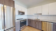 Located at 61 Fountain St in Framingham, Massachusetts, this single-floor unit offers a thoughtfully designed layout with contemporary finishes throughout. The open kitchen is a central highlight, featuring two-tone cabinetry with white upper cabinets and wood-grain lower cabinets, a white subway tile backsplash, light quartz countertops, and a full suite of stainless steel GE appliances including a range, built-in microwave, and dishwasher. Light wood-tone flooring runs consistently throughout the unit, creating a cohesive and modern aesthetic.

The living and bedroom areas are bright and open, benefiting from large floor-to-ceiling windows fitted with roller shades that offer views of the surrounding Framingham skyline. The neutral white walls and clean architectural lines contribute to a calm, contemporary ambiance throughout.

The unit includes two bathrooms. The primary bathroom features a double-sink vanity with a wide mirror, a glass-enclosed walk-in shower, and wood-look flooring. The secondary bathroom offers a single vanity and a soaking tub with a shower. Both bathrooms are finished with clean, modern fixtures and ample lighting, maintaining the unit's consistent contemporary character.