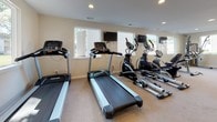 Located at 6741 E Tanners Creek Dr in Norfolk, Virginia, this well-equipped fitness center is housed in a single-floor facility designed to support a comprehensive workout experience. The space features a neutral-toned interior with light beige carpet flooring, recessed lighting throughout, and multiple windows fitted with louvered shutters that allow ample natural light to fill the room while providing views of the surrounding outdoor environment.

The cardio section is prominently appointed with multiple treadmills and elliptical machines, each positioned in front of wall-mounted flat-screen televisions for an engaging workout experience. The strength training area offers a multi-functional cable machine, adjustable weight benches, a dumbbell rack, and various resistance-based equipment to accommodate a range of exercise routines. Rowing machines are also available, providing additional low-impact cardio options.

A built-in water fountain station with an ADA-accessible unit is conveniently positioned along one wall, ensuring easy hydration access for all users. Wall-mounted mirrors help maximize the sense of space and assist users in monitoring their form. The facility also includes clearly marked exits and a clean, open layout that allows for safe and comfortable movement between equipment stations. Overall, this fitness center provides a practical and functional environment for residents to maintain an active lifestyle.