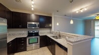 This single-floor unit offers a thoughtfully designed layout with a blend of modern finishes and functional spaces throughout. The entry foyer welcomes you with light tile flooring and a louvered storage closet, setting the tone for the well-maintained interior.

The kitchen serves as a standout feature, equipped with a full suite of stainless steel appliances including a refrigerator, electric range, built-in microwave, and dishwasher. Rich dark cabinetry extends to the ceiling, providing generous storage, while light granite countertops offer ample workspace. A double basin stainless steel sink sits along the peninsula, illuminated by elegant pendant lighting overhead. Light tile flooring completes the space.

The living and dining areas feature rich dark hardwood flooring, neutral walls, crown molding, and ceiling fans, creating a polished and comfortable atmosphere. A sliding glass door leads out to a balcony, allowing natural light to fill the room and offering outdoor views of surrounding greenery.

The bedroom is finished with plush carpeting, a ceiling fan, and a window framing lush tree views, contributing to a calm and restful setting.

The bathroom includes a full tub and shower combination with white subway tile surround, brushed bronze fixtures, and light tile flooring, offering a clean and classic aesthetic.