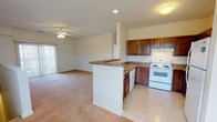 This single-floor residence is designed with an open-concept layout that seamlessly connects the kitchen and living area. The kitchen is well-appointed with rich medium-toned wood cabinetry, granite-look countertops, and white appliances including an electric range, dishwasher, and refrigerator. A peninsula with a breakfast bar separates the kitchen from the living space, which features light neutral carpet, recessed lighting, and a ceiling fan. Sliding glass doors in the living area provide natural light and outdoor access.

The bedrooms are carpeted and finished with neutral walls, offering a calm and functional environment. One bedroom benefits from a large window that allows ample natural light, while another features direct outdoor views. A generously sized walk-in closet is outfitted with wire shelving and hanging rods on multiple walls, providing extensive storage capacity.

The bathroom includes a full tub-shower combination with chrome fixtures, a toilet, and a vanity with granite-look countertops and wood cabinetry. Tile flooring runs through the kitchen and bathroom, while soft carpet covers the living and bedroom areas, giving the overall space a comfortable, cohesive feel.