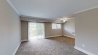 This single-floor, 1-bedroom, 1-bathroom unit offers a thoughtfully organized layout across a compact yet efficiently utilized footprint. The living room serves as the central gathering space, featuring warm neutral-toned carpet, crown molding, a ceiling fan with light fixture, and a large sliding glass door flanked by vertical blinds that opens to an outdoor balcony. A secondary window allows additional natural light and greenery views, creating a bright and welcoming ambiance.

The galley-style kitchen is positioned off the living area and is well-equipped with warm wood cabinetry, granite-style countertops with a breakfast bar overhang, track lighting, a gas range, and a black refrigerator. Light wood-look flooring lines the kitchen floor, providing a clean contrast to the surrounding carpeted rooms.

The bedroom is a generously sized private retreat with its own ceiling fan, a wide window with blinds offering natural light and outdoor views, and plush carpeting throughout. A dedicated closet provides practical storage, while a hallway connects the main areas of the unit. The bathroom features a full tub-shower combination with white subway tile surround, a vanity with sink, and a mirrored medicine cabinet, maintaining a clean and classic aesthetic throughout.