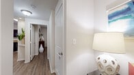 This single-floor residence is designed with a cohesive, modern aesthetic throughout. Wood-style plank flooring runs continuously across the main living areas, hallways, and bedrooms, creating a unified and easy-to-maintain foundation. Crisp white trim and neutral wall tones provide a clean backdrop, while an accent wall in the living room adds a touch of color.

The living area is well-proportioned, featuring a ceiling fan, white window blinds that allow controlled natural light, and ample room for varied furniture arrangements. Adjacent to the living space is a dedicated dining area with clear sightlines into the hallway and kitchen beyond.

The kitchen is equipped with dark espresso cabinetry, granite-style countertops, black appliances including a refrigerator, range, and dishwasher, and a window above the sink for natural light.

The bedroom is generously sized with a ceiling fan, a window with blinds, and direct access to the bathroom. The bathroom features dark cabinetry with a granite countertop, a large mirror, and a combination tub and shower.

Additional highlights include a walk-in closet with wire shelving and hanging rods, an in-unit laundry area with overhead shelving, and well-lit hallways connecting all areas of the home.