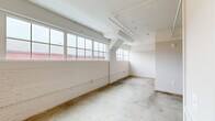 Located at 2154 Noisette Blvd in North Charleston, SC, this single-floor unit blends industrial character with modern updates throughout its thoughtfully arranged layout. Polished concrete floors run continuously through the space, complementing the exposed ductwork and structural beams overhead that nod to the building's industrial heritage. Whitewashed brick walls add texture and warmth, while large multi-pane windows invite generous natural light into the open living area, offering views of the surrounding neighborhood.

The kitchen is well-appointed with white shaker cabinetry, open shelving, marble-look countertops, a subway tile backsplash, and stainless steel appliances including a refrigerator, electric range, built-in microwave, and dishwasher. A single-basin sink with a matte black bridge faucet adds a refined, classic touch.

The bedroom features a ceiling fan, built-in closet storage, and exposed ceiling details consistent with the unit's industrial aesthetic. A corridor with a slatted louvered door provides functional storage or utility access.

The bathroom is clean and contemporary, finished with white subway tile in the glass-enclosed shower, black hardware accents, and a classic mosaic tile floor with a dark border detail, creating a crisp, timeless look throughout.