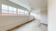 Located at 2154 Noisette Blvd in North Charleston, SC, this single-floor unit blends industrial character with modern updates throughout its thoughtfully arranged layout. Polished concrete floors run continuously through the space, complementing the exposed ductwork and structural beams overhead that nod to the building's industrial heritage. Whitewashed brick walls add texture and warmth, while large multi-pane windows invite generous natural light into the open living area, offering views of the surrounding neighborhood.

The kitchen is well-appointed with white shaker cabinetry, open shelving, marble-look countertops, a subway tile backsplash, and stainless steel appliances including a refrigerator, electric range, built-in microwave, and dishwasher. A single-basin sink with a matte black bridge faucet adds a refined, classic touch.

The bedroom features a ceiling fan, built-in closet storage, and exposed ceiling details consistent with the unit's industrial aesthetic. A corridor with a slatted louvered door provides functional storage or utility access.

The bathroom is clean and contemporary, finished with white subway tile in the glass-enclosed shower, black hardware accents, and a classic mosaic tile floor with a dark border detail, creating a crisp, timeless look throughout.