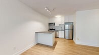 This thoughtfully designed 1-bedroom, 1-bathroom unit offers a smart and efficient layout across a single floor. Light wood laminate flooring runs throughout the space, creating a clean and cohesive aesthetic. The combined kitchen and living area forms the heart of the unit, with the kitchen showcasing white shaker-style cabinetry, a herringbone-pattern tile backsplash, dark countertops, and a full suite of stainless steel appliances including a range, dishwasher, over-the-range microwave, and refrigerator. The bedroom is a comfortable, well-proportioned room featuring a classic cast-iron radiator beneath a wide window that frames views of surrounding greenery, filling the space with natural light. A double-door closet provides ample storage. The bathroom is finished in crisp white subway tile from floor to ceiling, complemented by a white vanity with an undermount sink, a quartz countertop, and a shower-tub combination with chrome fixtures. Neutral white walls throughout the unit contribute to a bright, airy ambiance, while the traditional radiator heating system adds a touch of classic character to the otherwise modern, updated interior.