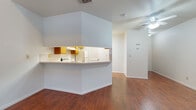This two-floor residence is defined by rich hardwood flooring that flows seamlessly throughout every room, creating a warm and cohesive aesthetic. The kitchen is well-appointed with honey-toned wood cabinetry, white countertops, a double stainless steel sink, a coil-top range, and ample upper and lower storage. A pass-through counter opening connects the kitchen to the living area, promoting an open and communicative layout. The living and dining areas are generously proportioned, bathed in natural light from a bank of tall vertical windows that frame outdoor views. Ceiling fans are installed throughout, offering both comfort and light. A lofted upper level is accessible via stairway, featuring an open railing overlook with pendant lighting that adds architectural interest. The primary bedroom benefits from vaulted ceilings, a ceiling fan, and a walk-in closet. The bathroom includes a wide vanity with wood cabinetry, a large mirror, and wall-mounted storage cabinets. Crisp white walls throughout the home provide a clean, neutral backdrop that complements the warmth of the wood floors and cabinetry. The overall ambiance is functional, bright, and inviting.