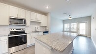 This single-story residence in South Fulton, Georgia, presents a clean, contemporary design with a neutral color palette and quality finishes throughout. The open-concept kitchen is a central highlight, showcasing crisp white shaker cabinetry, granite countertops, a subway tile backsplash, and a generously sized center island that provides additional prep space and casual seating. Stainless steel appliances, including a refrigerator, electric range, microwave, and dishwasher, complete the kitchen's modern aesthetic. Light wood-style flooring runs through the main living and kitchen areas, contributing to a bright, cohesive feel.

The living area flows naturally from the kitchen, offering ceiling fan fixtures and windows that allow natural light to fill the space. Bedrooms feature plush carpeting, ceiling fans, and windows with views of the surrounding community. At least one bedroom includes a dedicated closet with built-in shelving, providing organized storage. The bathroom features a granite-topped vanity, wood-look flooring, and a tiled shower surround. A dedicated laundry area accommodates a full-size washer and dryer, adding everyday convenience to this well-appointed residence.