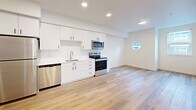 Located on the third floor at 1245 N Anchor Way in Portland, Oregon, this contemporary one-bedroom, one-bathroom unit offers a well-designed layout with modern finishes throughout. Light-toned hardwood-style flooring runs continuously through all rooms, creating a cohesive and airy feel.

The open kitchen is outfitted with crisp white cabinetry extending to the ceiling, stainless steel appliances including a full-size refrigerator, electric range, built-in microwave, dishwasher, and a single-basin sink. A subtle tile backsplash and recessed lighting complete the clean, functional aesthetic. A distinctive circular porthole-style window adds a unique architectural touch to the kitchen and living area.

The living area flows naturally from the kitchen, benefiting from additional natural light provided by a large picture window with neighborhood views.

The bedroom is a well-proportioned private retreat featuring a large window that fills the room with natural light. Two closets provide ample storage throughout the unit.

The bathroom maintains the home's modern design language with white cabinetry, a wide vanity with a solid surface countertop, a full soaking tub with shower, and coordinating black hardware accents. Recessed lighting keeps the space feeling bright and clean. The unit's consistent palette of white walls and warm flooring lends a fresh, move-in-ready atmosphere.