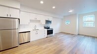 Located on the third floor at 1245 N Anchor Way in Portland, Oregon, this contemporary one-bedroom, one-bathroom unit offers a well-designed layout with modern finishes throughout. Light-toned hardwood-style flooring runs continuously through all rooms, creating a cohesive and airy feel.

The open kitchen is outfitted with crisp white cabinetry extending to the ceiling, stainless steel appliances including a full-size refrigerator, electric range, built-in microwave, dishwasher, and a single-basin sink. A subtle tile backsplash and recessed lighting complete the clean, functional aesthetic. A distinctive circular porthole-style window adds a unique architectural touch to the kitchen and living area.

The living area flows naturally from the kitchen, benefiting from additional natural light provided by a large picture window with neighborhood views.

The bedroom is a well-proportioned private retreat featuring a large window that fills the room with natural light. Two closets provide ample storage throughout the unit.

The bathroom maintains the home's modern design language with white cabinetry, a wide vanity with a solid surface countertop, a full soaking tub with shower, and coordinating black hardware accents. Recessed lighting keeps the space feeling bright and clean. The unit's consistent palette of white walls and warm flooring lends a fresh, move-in-ready atmosphere.