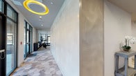 Located at 793 Post Rd E in Westport, Connecticut, this single-floor fitness facility offers a thoughtfully designed space that balances modern aesthetics with full workout functionality. The main exercise area is anchored by floor-to-ceiling glass walls that flood the room with natural light and provide open views of the surrounding streetscape, creating an energizing atmosphere for users.

The gym is outfitted with a comprehensive range of equipment, including treadmills, stationary cycling bikes, a dumbbell rack, stability balls, medicine balls in varying weights, resistance bands, and a wall-mounted display screen. A large floor-to-ceiling mirror panel visually expands the workout space while allowing users to monitor their form. Recessed ceiling lighting complements the abundant natural light throughout.

A dedicated corridor connects the workout areas and features distinctive textured wave-patterned wall panels alongside a bold circular yellow ceiling fixture, lending a polished, design-forward character to the space. The flooring transitions thoughtfully between areas, with geometric herringbone-patterned tile in the corridor and plush carpet in the main exercise zones.

The facility also includes an accessible restroom finished with large-format hexagonal wood-look wall tiles and polished stainless steel grab bars, combining style with practicality. Overall, the space presents a clean, contemporary fitness environment suited for a professional or residential community setting.