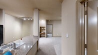 Located on Vance Jackson Road in San Antonio, Texas, this single-floor residence offers a well-designed layout with two bedrooms, two bathrooms, and a generous overall footprint. The kitchen is fitted with light wood cabinetry, granite-style countertops, a breakfast bar peninsula, and black appliances including a refrigerator, range, and dishwasher. Light hardwood-style flooring runs through the kitchen, transitioning to plush carpet in the living and bedroom areas. The primary bedroom is a spacious retreat featuring a ceiling fan, a large window that invites natural light, and access to a walk-in closet outfitted with dual hanging rods and multiple shelving tiers for ample storage. A second walk-in closet mirrors this practical design. The primary bathroom is notably expansive, featuring a double-sink vanity with warm wood cabinetry and stone-look countertops, tile flooring, and a shower-tub combination. The second bathroom offers a single vanity with matching finishes and a tub-shower combo. Additional highlights include a dedicated in-unit laundry area housing a full-size washer, a private balcony, and neutral warm-tone walls throughout that lend a cohesive, inviting ambiance across the entire space.