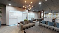 Located on Chandler Boulevard in Los Angeles, this single-floor commercial amenity space offers a thoughtfully designed interior that balances comfort and contemporary style. The layout flows across several distinct zones, each serving a unique function while maintaining a cohesive modern aesthetic throughout.

The main lounge area is anchored by plush gray sofas and dark leather armchairs arranged around low coffee tables, creating an inviting setting for relaxed gathering. Large frosted windows line the walls, filtering soft natural light and offering silhouetted views of palm trees beyond. A striking sputnik chandelier serves as a focal point overhead, complementing the dark drop-tile ceiling and recessed lighting throughout.

Wood-paneled columns and accent walls add warmth and visual depth, transitioning into a bar-style seating area with a white countertop island, pendant lights, and walnut-toned cabinetry. A game room features a pool table, bar-height seating, and a bold geometric accent wall in gold and white. A kitchenette with a sink and built-in cabinetry supports the entertaining function of this area.

A media lounge with a wall-mounted flat-screen TV, built-in shelving, and tall indoor plants rounds out the space, offering a relaxed viewing environment. Light wood-look flooring and neutral tones unify the entire space.