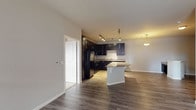 Located at 5101 S Rio Grande St in Littleton, Colorado, this single-floor residence offers a thoughtfully designed layout with modern finishes and a cohesive aesthetic throughout. The open-concept kitchen and living area serves as the heart of the home, anchored by rich dark cabinetry with sleek hardware, granite-style countertops, and a curved breakfast bar island that provides additional seating and workspace. A full suite of black appliances includes a refrigerator, range, microwave, and dishwasher. Track lighting and a pendant fixture provide layered illumination over the kitchen, complemented by warm wood-look luxury vinyl plank flooring that extends across the main living areas. The bedrooms are carpeted for comfort and offer generous proportions, with one featuring direct access to a walk-in closet equipped with wire shelving for organized storage. The bathrooms echo the kitchen's design language with matching dark vanity cabinetry, granite-style countertops, and wood-look flooring. Each bathroom includes a full soaking tub with shower, and one bathroom provides convenient direct access to a closet. Neutral wall tones throughout the space create a clean, versatile backdrop suited to a variety of interior styles.
