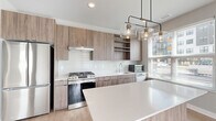 Located at 365 S Moorland Rd in Brookfield, WI, this thoughtfully designed 2-bedroom, 3-bathroom residence offers a clean, contemporary aesthetic across a well-organized single-floor layout. The open-concept kitchen and living area serves as the heart of the home, showcasing flat-panel wood-toned cabinetry, a crisp white subway tile backsplash, stainless steel appliances, and a large quartz island perfect for dining or entertaining. An industrial-style pendant light cluster adds character overhead, while generous windows flood the space with natural light. Light wood-tone luxury vinyl plank flooring runs throughout the main living areas, lending warmth and continuity. The hallway connects the living space to the bedrooms with a smooth, open flow. The spacious primary bedroom features plush carpeting, a large window with outdoor views, and access to a walk-in closet equipped with wire shelving. The bathrooms are finished with wood-tone vanities, white quartz countertops, large mirrors, and clean white tile tub-shower combinations with chrome fixtures. The second bedroom also offers carpeted flooring and ample natural light. Additional highlights include a dedicated laundry room, a utility room, and two well-appointed closets, providing excellent storage solutions throughout this well-appointed Brookfield residence.