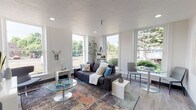 Located at 1216 N Superior St in Spokane, WA, this single-floor unit offers a well-designed, modern living environment with a cohesive aesthetic throughout. The living area is bright and open, benefiting from multiple large windows that flood the space with natural light and provide views of the surrounding greenery. The room comfortably accommodates both a seating area and a dining nook, with light wood-tone flooring and recessed lighting lending a clean, contemporary feel. The galley-style kitchen is thoughtfully laid out with ample storage provided by floor-to-ceiling grey cabinetry featuring sleek bar-pull hardware. White quartz countertops run the full length of both sides, offering generous workspace, while stainless steel appliances — including a refrigerator, range, and microwave — complete the functional setup. Light wood-grain flooring carries through the space seamlessly. The bathroom is bright and efficiently designed, featuring a full soaking tub and shower combination with a classic tile surround, a grey vanity with a white countertop, and wood-tone flooring that ties back to the rest of the unit. The overall layout, as seen in the dollhouse view, connects the living, sleeping, kitchen, and bathroom areas in a practical, open-concept arrangement ideal for everyday living.
