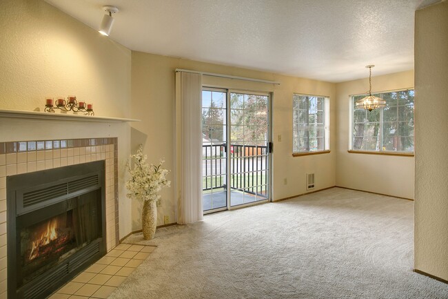 A spacious living room with a fireplace, a view into the dining area, and large sliding glass doors that lead out to the private balcony - Heron View