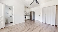 This 230 square foot studio apartment in Los Angeles offers a thoughtfully designed living space that maximizes functionality in a compact footprint. The modern kitchen is equipped with sleek stainless steel appliances, including a full-size refrigerator, range, and over-the-range microwave. White shaker-style cabinets provide ample storage and are complemented by a subway tile backsplash, creating a clean and contemporary aesthetic.

The main living area features light-toned wood-look flooring that extends throughout the space, enhancing the sense of openness. Large windows allow natural light to flood the room, while a modern ceiling fan ensures good air circulation. The bathroom, though not fully visible in the images, appears to have a white tiled shower with modern fixtures.

The apartment's design makes efficient use of vertical space with tall cabinets and high ceilings. The neutral color palette, dominated by whites and light grays, contributes to a bright and airy ambiance. Despite its small size, the apartment offers all essential amenities in a well-organized layout, making it an ideal option for urban living in the heart of Los Angeles.