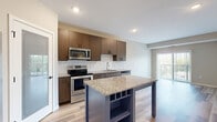 This well-appointed one-bedroom, one-bathroom unit at 15315 Maple Island Rd in Burnsville, MN offers a thoughtfully designed single-floor layout. The open-concept kitchen and living area serves as the heart of the home, showcasing warm wood cabinetry, granite countertops, a classic subway tile backsplash, and a full suite of stainless steel appliances including a refrigerator with ice maker, range, microwave, and dishwasher. A distinctive blue kitchen island with built-in shelving and a granite top provides additional prep space and storage. Light hardwood-style flooring runs throughout the main living areas, complementing the neutral wall tones. The living room opens to a private balcony through a sliding glass door, allowing natural light to fill the space and offering pleasant outdoor views. The bedroom features plush carpeting, a ceiling fan, and a window with natural light. A spacious walk-in closet with wire shelving provides generous storage. The bathroom is finished with a granite vanity, wood-toned cabinetry, and a full tub-shower combination. A dedicated pantry adds further practicality to this clean, modern unit.