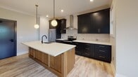 Located at 525 Ridge St in Charlottesville, Virginia, this single-floor unit showcases a thoughtfully designed interior with modern finishes and a cohesive aesthetic throughout. Light hardwood-style flooring runs continuously across the space, contributing to a bright and airy atmosphere enhanced by recessed lighting and natural light from well-placed windows with views of surrounding greenery.

The kitchen is a standout feature, boasting bold dark cabinetry with gold hardware contrasted by crisp white quartz countertops. A large center island with a warm wood base, an integrated sink with a matte black faucet, and globe pendant lighting make this space as functional as it is visually striking. A textured tile backsplash, stainless steel appliances, and a sleek wall-mounted range hood complete the culinary space.

The open living area flows seamlessly from the kitchen, offering generous proportions, crown molding, and a sliding barn door detail that adds a contemporary-rustic accent. Bedrooms are well-sized, with one featuring a ceiling fan, and another benefiting from natural light through a large window. In-unit laundry is conveniently accessible.

The bathroom is elegantly appointed with a floating wood vanity, white countertop, a gold-framed mirror, and a stylish sconce light fixture, complemented by a tiled shower enclosure visible in the background.