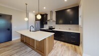 Located at 525 Ridge St in Charlottesville, Virginia, this single-floor unit showcases a thoughtfully designed interior with modern finishes and a cohesive aesthetic throughout. Light hardwood-style flooring runs continuously across the space, contributing to a bright and airy atmosphere enhanced by recessed lighting and natural light from well-placed windows with views of surrounding greenery.

The kitchen is a standout feature, boasting bold dark cabinetry with gold hardware contrasted by crisp white quartz countertops. A large center island with a warm wood base, an integrated sink with a matte black faucet, and globe pendant lighting make this space as functional as it is visually striking. A textured tile backsplash, stainless steel appliances, and a sleek wall-mounted range hood complete the culinary space.

The open living area flows seamlessly from the kitchen, offering generous proportions, crown molding, and a sliding barn door detail that adds a contemporary-rustic accent. Bedrooms are well-sized, with one featuring a ceiling fan, and another benefiting from natural light through a large window. In-unit laundry is conveniently accessible.

The bathroom is elegantly appointed with a floating wood vanity, white countertop, a gold-framed mirror, and a stylish sconce light fixture, complemented by a tiled shower enclosure visible in the background.