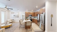 This single-story, 2-bedroom, 2-bathroom home offers a thoughtfully designed layout that maximizes its footprint with a clean, contemporary aesthetic. The open-concept kitchen and living area serves as the heart of the home, featuring warm wood-toned flat-front cabinetry, a full suite of stainless steel appliances including a French door refrigerator, electric range, and built-in microwave. A white waterfall-edge kitchen island with bar seating provides a natural gathering space that flows seamlessly into the living area, which benefits from natural light through large windows with blinds and a ceiling fan overhead. Light wood-style flooring runs throughout the main living spaces, enhancing the bright, airy atmosphere. Both bedrooms are carpeted and well-proportioned, with the primary bedroom featuring a window that invites natural light, and the second bedroom equipped with a ceiling fan and recessed lighting. Each bathroom is finished with clean white surrounds, wood-front vanities with white countertops, and light wood flooring, with one bathroom offering a full soaking tub and shower combination. The overall design maintains a cohesive modern-neutral palette throughout, offering a comfortable and functional living environment.