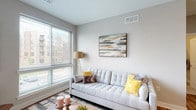 This well-appointed single-floor residence offers a thoughtfully designed layout that balances comfort and contemporary style throughout. The living room serves as the heart of the home, bathed in natural light from large windows fitted with blinds that frame views of the surrounding landscape. Warm hardwood flooring, neutral-toned walls, and a balcony door enhance the open, airy feel of the space.

The kitchen is a standout feature, showcasing white shaker cabinetry extending to the ceiling, a classic subway tile backsplash, grey quartz countertops, and a full suite of stainless steel appliances including a gas range, microwave, dishwasher, and refrigerator. A generously sized center island with bar seating and pendant lighting overhead makes it ideal for both cooking and casual dining.

The primary bedroom offers a serene retreat with plush carpeting, a ceiling fan, and access to a walk-in closet. Its ensuite bathroom features white cabinetry, grey quartz countertops, and a walk-in shower. A second bedroom, equally well-sized with soft carpeting, is served by a second full bathroom with a tub-shower combination and matching finishes. The cohesive design palette of soft greys, whites, and warm wood tones flows seamlessly throughout the entire residence.
