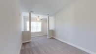 This single-floor, one-bedroom, one-bathroom residence is part of Phase II of the Autumn community and includes a desirable sunroom addition. The living area is finished with soft, neutral-toned carpeting and features vaulted ceilings that lend an open, airy feel to the space. Architectural column details frame the transition between the living and adjacent areas, adding a touch of structural character. A ceiling fan provides both comfort and subtle style overhead. Natural light flows generously through white-slatted blinds on double windows, brightening the interior with a clean, welcoming ambiance. The walls are painted in a warm, neutral tone throughout, creating a cohesive and calming atmosphere. The entryway, visible from the main living space, offers a classic paneled door and easy access to the rest of the home. The inclusion of a sunroom extends the livable space further, providing an ideal spot for relaxation or additional versatility. Ceiling vents are well-positioned for efficient climate control. Overall, the residence presents a tidy, move-in-ready environment with thoughtful design details suited for comfortable everyday living.