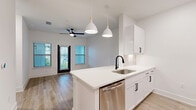 This thoughtfully designed 1-bedroom, 1-bathroom unit offers a clean, modern aesthetic with an open-concept floor plan that maximizes every inch of its well-utilized footprint. The kitchen serves as a central focal point, featuring a large white quartz peninsula with an undermount sink and matte black faucet, crisp white shaker cabinetry with black hardware, and a full suite of stainless steel appliances including a gas range, dishwasher, refrigerator, and microwave. Stylish pendant lights hang above the peninsula, complementing the contemporary design. The kitchen flows seamlessly into the living area, which benefits from natural light streaming through multiple windows and is equipped with a ceiling fan. Light-toned wood-look flooring runs consistently throughout the entire unit, enhancing the sense of openness and continuity. The bedroom is a bright, comfortable retreat with double windows overlooking greenery, a ceiling fan, and direct access to both a dedicated closet and the bathroom. The bathroom maintains the same refined palette with white cabinetry, quartz countertops, a framed mirror, and matte black accents, with tile detailing in the shower area. The overall ambiance is clean, bright, and move-in ready.