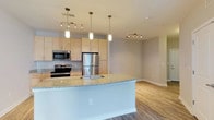 This well-appointed 1-bedroom unit is designed with a modern, open-concept layout that seamlessly connects the kitchen and living areas into a cohesive, functional living space. The kitchen serves as the focal point, centered around a large island with a granite countertop and an undermount stainless steel sink. Elegant pendant lights hang above the island, adding a warm, contemporary touch. Light wood cabinetry provides ample storage, while a full suite of stainless steel appliances — including a refrigerator, range, and microwave — delivers a sleek, polished finish. Track lighting throughout the kitchen and living areas ensures the space is well-lit and versatile. The open living area extends naturally from the kitchen, featuring hardwood-style flooring that runs throughout the unit, contributing to a clean and cohesive aesthetic. A ceiling fan with a light fixture adds both comfort and functionality to the living space. Large windows invite natural light and provide a view to the outdoors, enhancing the bright and airy atmosphere. Neutral-toned walls and crisp white trim complete the modern, move-in-ready feel of this thoughtfully designed single-floor residence.