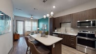 This thoughtfully designed single-floor residence combines contemporary style with functional living. The open-concept layout connects the kitchen and living area seamlessly, creating a welcoming, social atmosphere. The kitchen is outfitted with rich dark wood cabinetry, a light quartz countertop island with pendant lighting overhead, a subway tile backsplash, and a full suite of stainless steel appliances including a refrigerator, range, microwave, and dishwasher. Wood-look flooring runs throughout the main living areas, adding warmth and cohesion to the space.

The living area is defined by a striking teal accent wall that serves as a vibrant focal point, complemented by large windows that invite natural light. The bedroom continues the teal accent wall detail in at least one room, paired with generous windows dressed in striped sheer curtains, creating a bright and restful retreat. A second bedroom offers a neutral palette with ample natural light.

The bathroom features a elongated vanity with dark wood cabinetry and a white countertop, wood-look flooring, a full soaking tub, and floor-to-ceiling tiled shower surround in a subtle stone-like pattern. Together, the finishes and design choices throughout this residence deliver a cohesive, modern aesthetic with distinctive pops of color and high-quality materials.