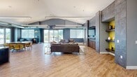 This 2,480 square foot single-floor space offers a contemporary communal environment. The open layout seamlessly blends multiple functional areas, including a spacious lounge with comfortable seating, a sleek kitchen with a large island and bar stools, and various seating arrangements for dining or working. Architectural highlights include high ceilings with exposed ductwork, pendant lighting, and large windows providing ample natural light. The decor combines neutral tones with pops of color, featuring modern furniture and a mix of flooring materials. A standout blue neon sign adds a unique touch to the ambiance. The space also includes amenities such as a TV area, outdoor access, and appears to be part of a larger complex with additional facilities.
