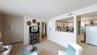This single-floor residence offers a thoughtfully designed layout that balances comfort and functionality. The living area is carpeted and open, providing a welcoming space for relaxation and entertaining. A pass-through window connects the living room to the kitchen, creating an airy, open feel while maintaining a sense of defined space. The kitchen is efficiently arranged in a U-shaped configuration, featuring warm wood-trimmed cabinetry with white panels, a double-basin sink, an electric range, an over-the-range microwave, and ample counter space — making it practical for everyday cooking. The bedroom is generously sized with plush carpeting and benefits from easy access to both a dedicated walk-in closet and an en-suite bathroom. The bathroom is equipped with a vanity featuring wood cabinetry, a sink, and well-lit mirror space. Throughout the residence, neutral tones on the walls and ceilings create a clean, cohesive aesthetic, while the consistent carpeting and trim details lend a sense of continuity. The overall ambiance is comfortable and functional, with a layout that maximizes the use of available space across the single floor.