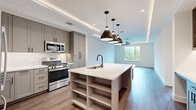 Located in Austin's sought-after 78704 neighborhood, this modern one-bedroom, one-bathroom residence offers a thoughtfully designed layout with contemporary finishes throughout. The open-concept living and kitchen area is a standout, anchored by a large central island with a white quartz countertop, integrated sink, and built-in shelving below. Gray shaker-style cabinetry lines the kitchen walls, complemented by stainless steel appliances including a gas range, French door refrigerator, built-in microwave, and dishwasher. Striking matte black pendant lights hang above the island, while recessed lighting and elegant tray ceilings with cove lighting add architectural depth to the space. Warm hardwood-style flooring flows seamlessly through the main living areas. The bedroom is generously proportioned, featuring French doors that open to a private balcony with lush outdoor views and a ceiling fan overhead, filling the room with natural light. The bathroom is spa-like in character, showcasing large-format tile flooring, a dual-sink vanity with gray cabinetry and matte black fixtures, a soaking tub, and a separate walk-in shower with marble-style tile surround. A dedicated closet completes this well-appointed residence.