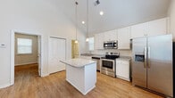 Located at 2314 Doveshell Dr in North Myrtle Beach, SC, this single-story home offers a clean, modern aesthetic with thoughtful design details throughout. The standout feature is the kitchen, which boasts soaring vaulted ceilings that create an impressive sense of openness and volume. Crisp white shaker-style cabinetry pairs elegantly with speckled granite countertops, while a central island provides additional workspace and casual gathering space. Stainless steel appliances — including a refrigerator with ice maker, range, microwave, and dishwasher — complete the well-appointed kitchen. Pendant lighting hangs above the island, adding warmth to the bright, window-lined space. Warm wood-look flooring runs consistently throughout the home, lending a cohesive and inviting feel to every room. The bedrooms are generously sized, with natural light filtering through slatted blinds; one bedroom features a tray ceiling detail with a ceiling fan. The bathroom is efficiently designed with a granite-topped vanity, a sliding-glass enclosed shower, and matching wood-look flooring. A dedicated laundry area houses a stacked washer and dryer unit with adjacent shelving for added convenience. The home's light-filled, neutral palette and consistent finishes make it a practical and attractive residence in the North Myrtle Beach area.